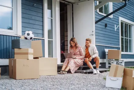 Junger Mann und Frau sitzen auf einer Veranda ihres neuen Zuhauses und benutzen einen Laptop