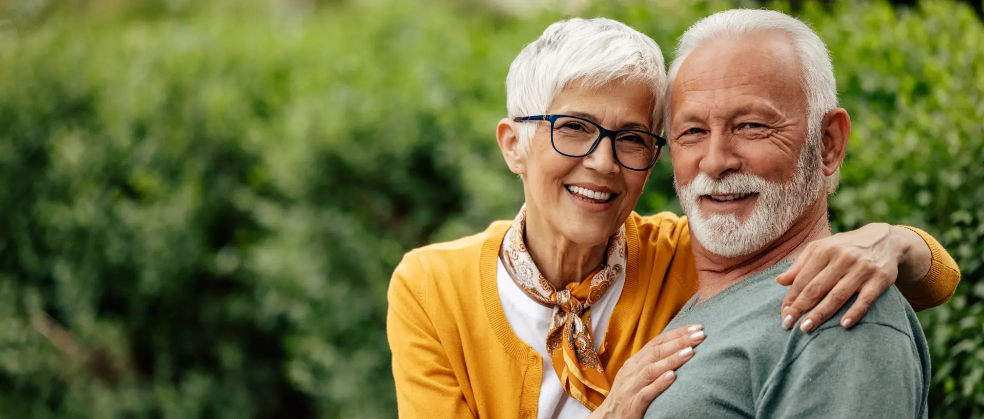 Zwei Senioren sitzen glücklich auf einer Bank im Grünen