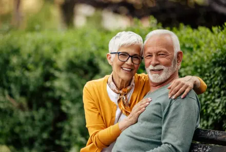 Zwei Senioren sitzen glücklich auf einer Bank im Grünen