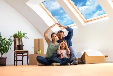 Junge moderne Familie mit Kind sitzt auf dem Boden unter dem Dachfenster ihrer neuen Wohnung