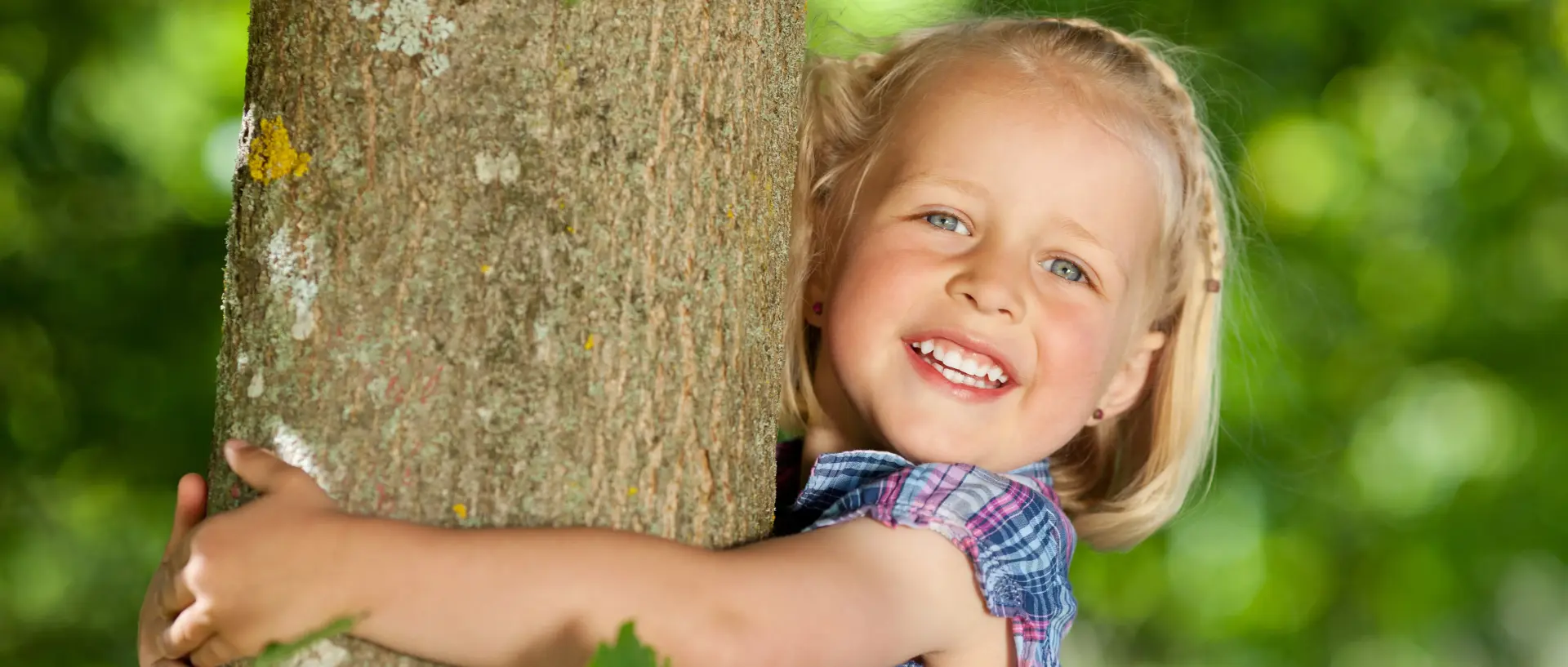 Kleines Mädchen umarmt einen Baum und lächelt in die Kamera