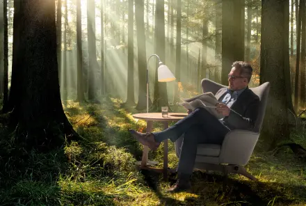 Mann sitzt in einem Sessel im Wald und liest ganz entspannt Zeitung