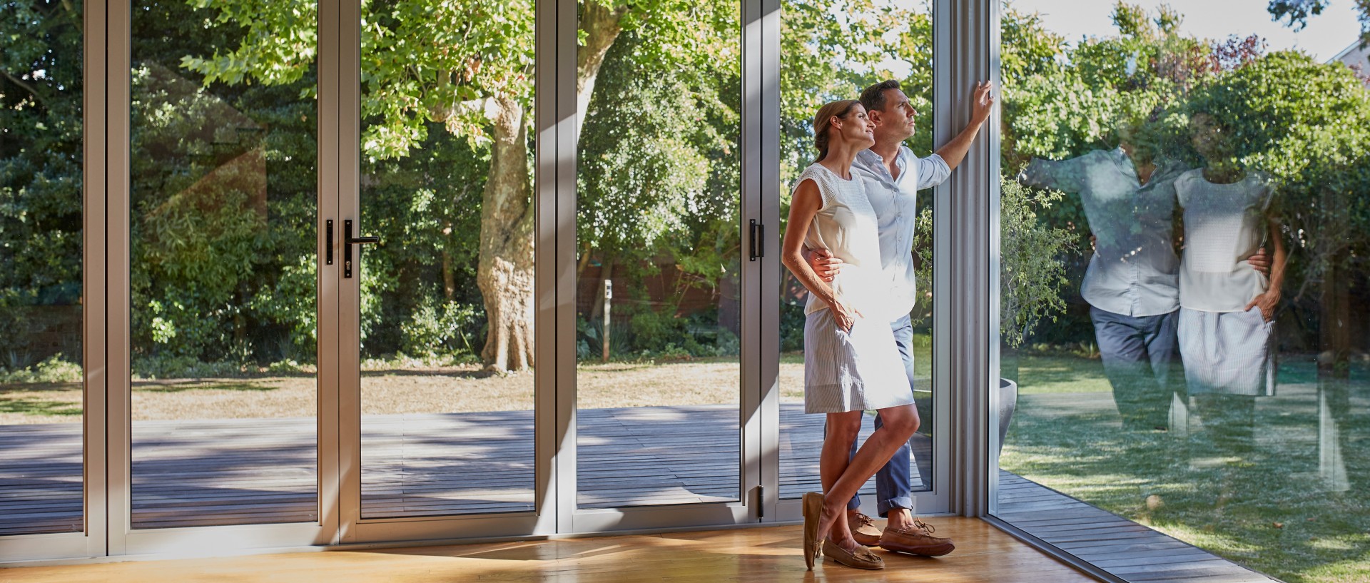 Mittelerwachsenes Paar schaut durch ihre großen Glasfenster in den Garten