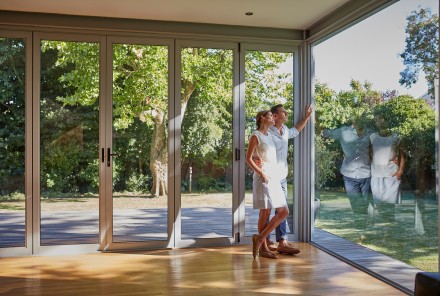 Mittelerwachsenes Paar schaut durch ihre großen Glasfenster in den Garten
