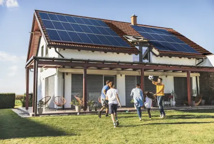 Familie spielt Ball vor einem Haus mit Solaranlage auf dem Dach