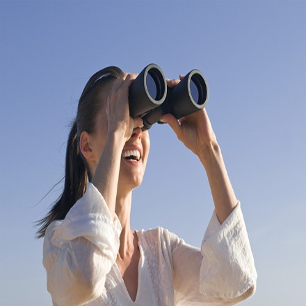 Frau schaut mit Fernglas in die Ferne