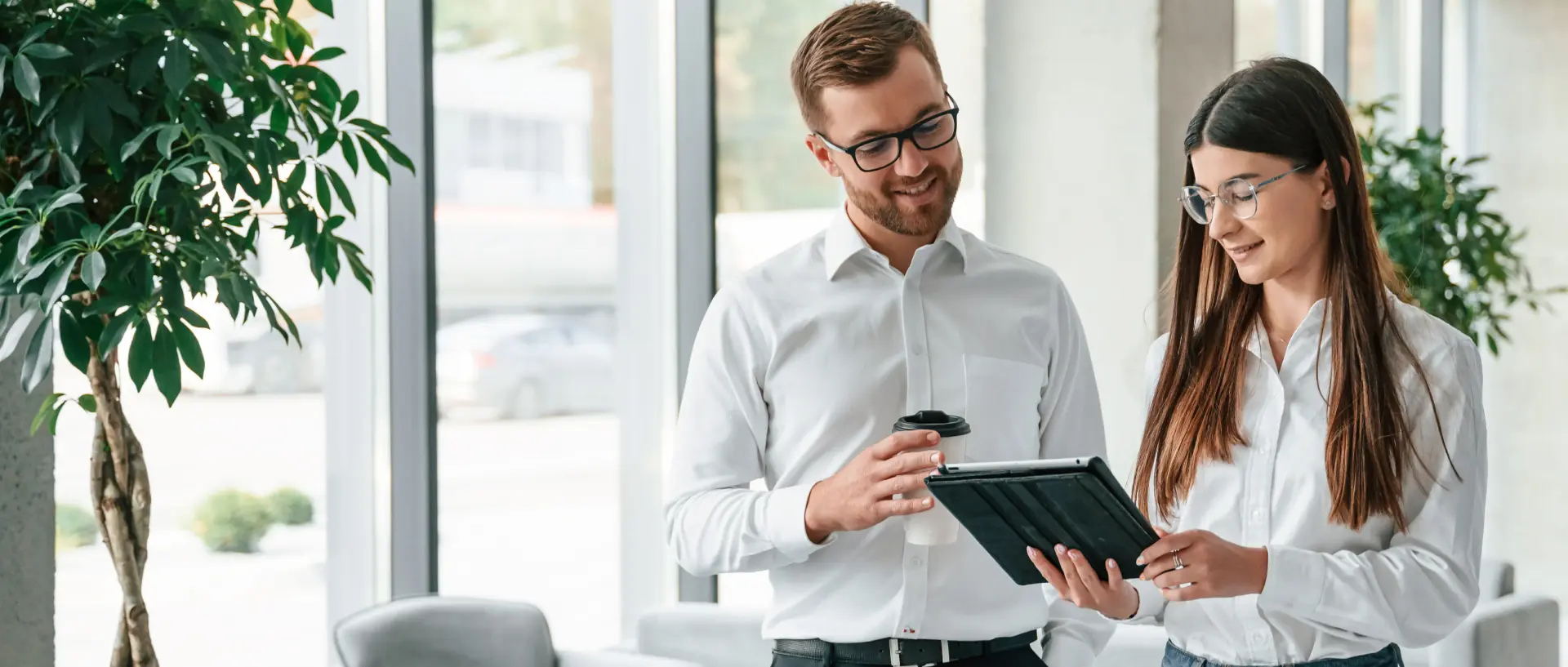 Zwei junge Menschen stehen im Büro und schauen in ein Tablet