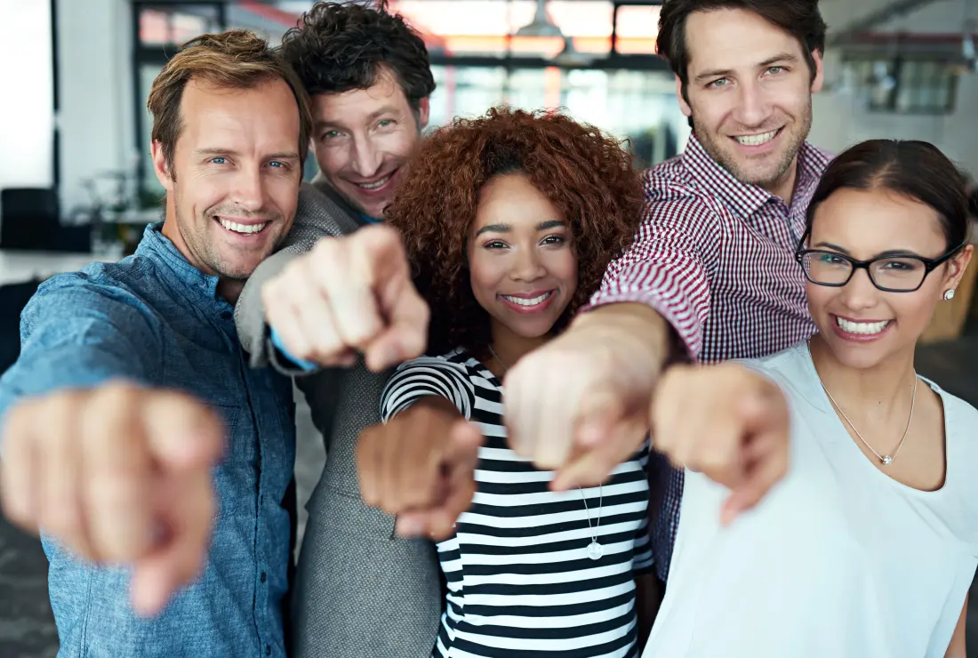 Fröhliche Menschen im Büro zeigen mit Fingern in die Kamera